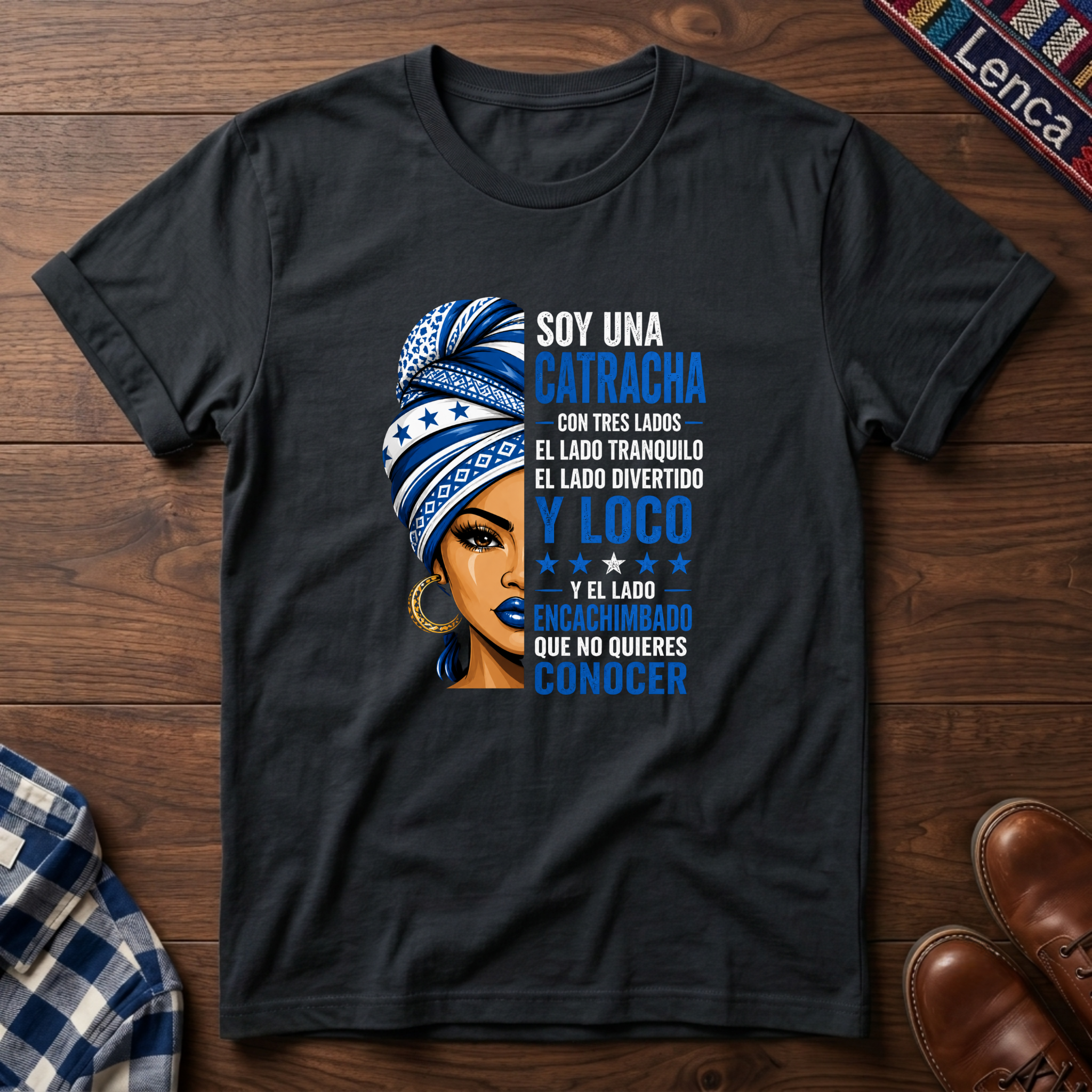 Black  t-shirt with a graphic of a woman with a headwrap and 'Soy Una Catracha' text on a wooden surface.