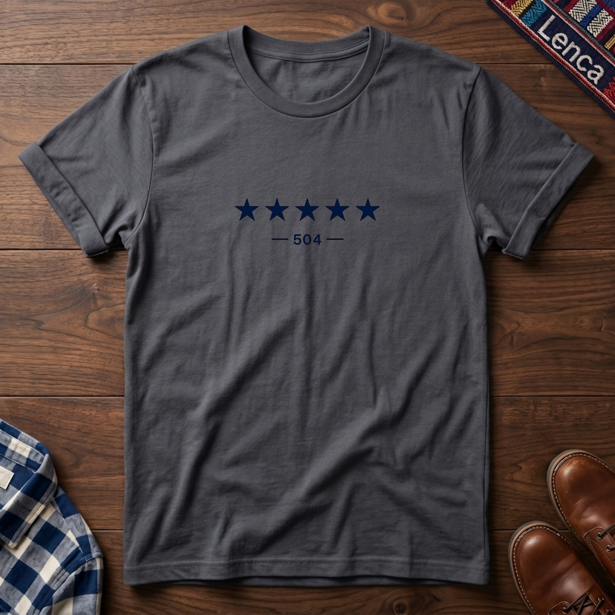A charcoal short-sleeve crewneck t-shirt with a graphic of five dark blue stars and the text '— 504 —' on the chest, laid flat on a wooden surface.
