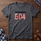 A charcoal t-shirt laid flat on a wooden surface, featuring the text 'HONDURAS 504' printed on the chest. The numbers '504' are filled with a red, white, and blue pattern resembling the Honduran Lempira, while 'HONDURAS' is printed in black.