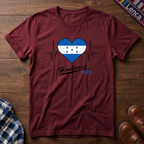 Cherry red t-shirt with a heart design featuring Honduras' flag and 'Honduras 100%' text on a wooden surface.
