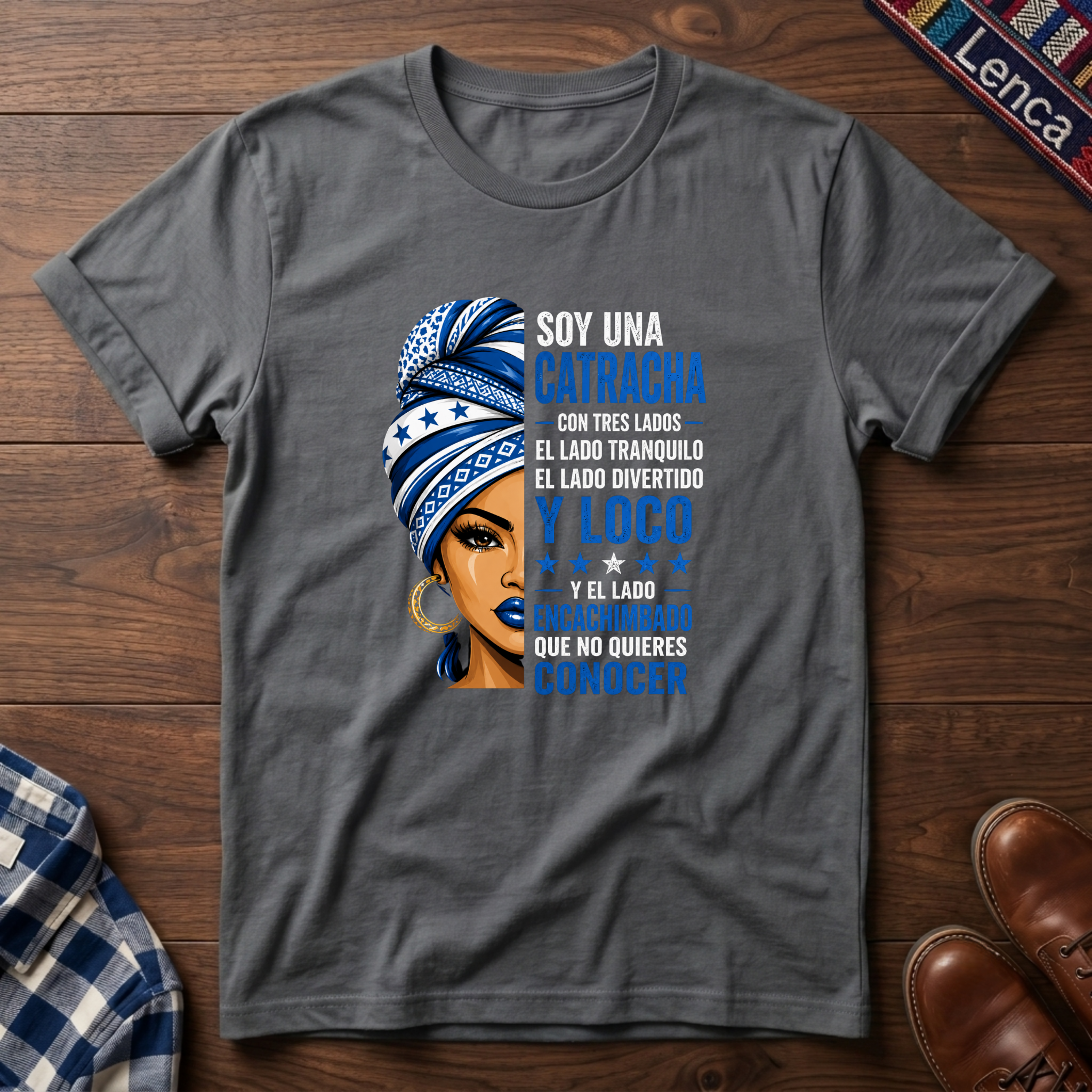 Graphite Heather t-shirt with a graphic of a woman with a headwrap and 'Soy Una Catracha' text on a wooden surface.