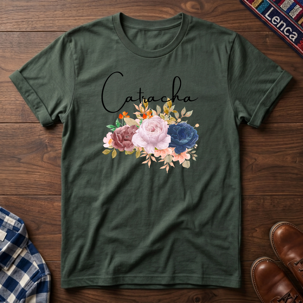 Military green short-sleeve crewneck t-shirt laid flat on a dark wood background, featuring the name 'Catacha' in black script above a watercolor floral design with pink, blue, and peach flowers.