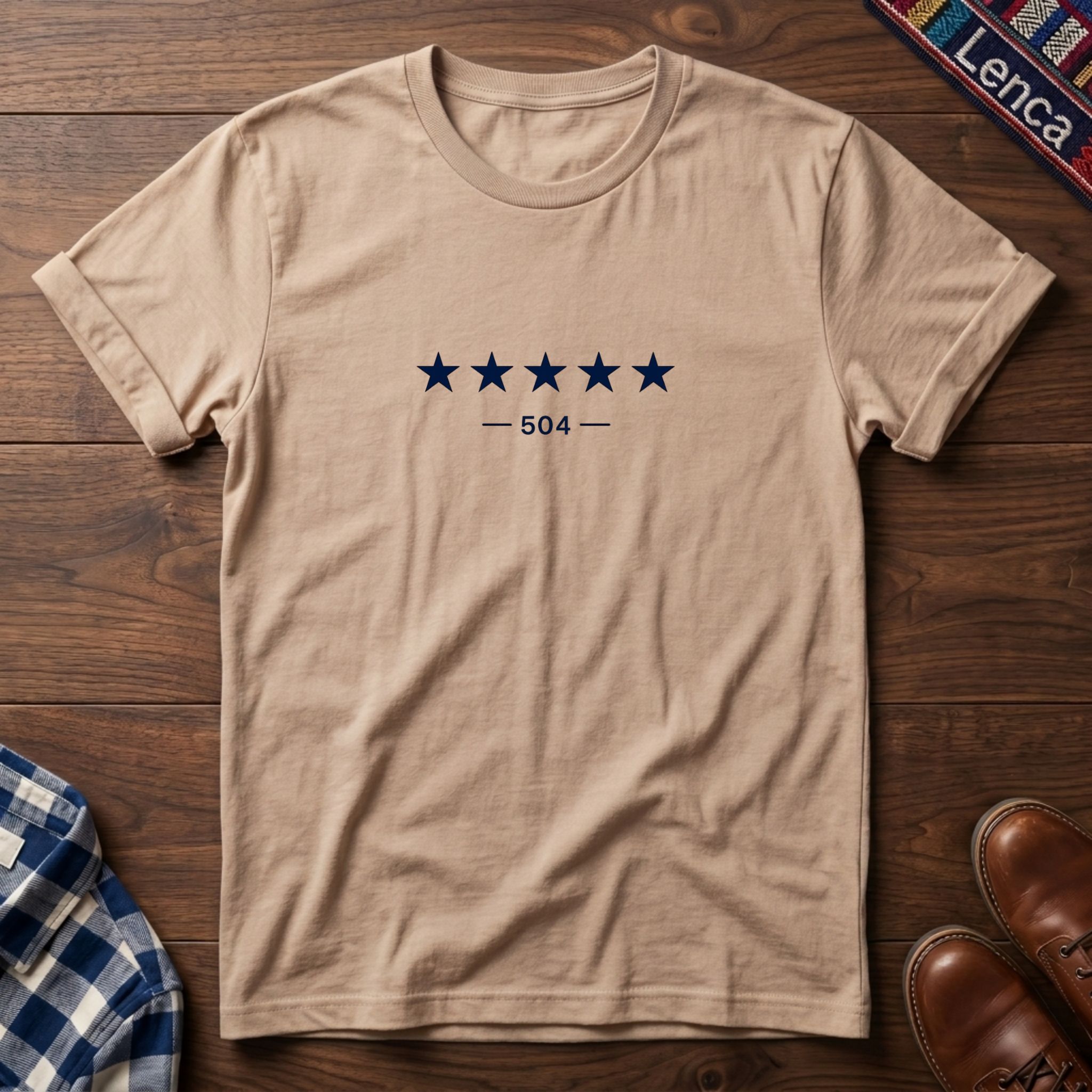 Natural short-sleeve crewneck t-shirt with a graphic of five dark blue stars and the text '— 504 —' on the chest, laid flat on a wooden surface.