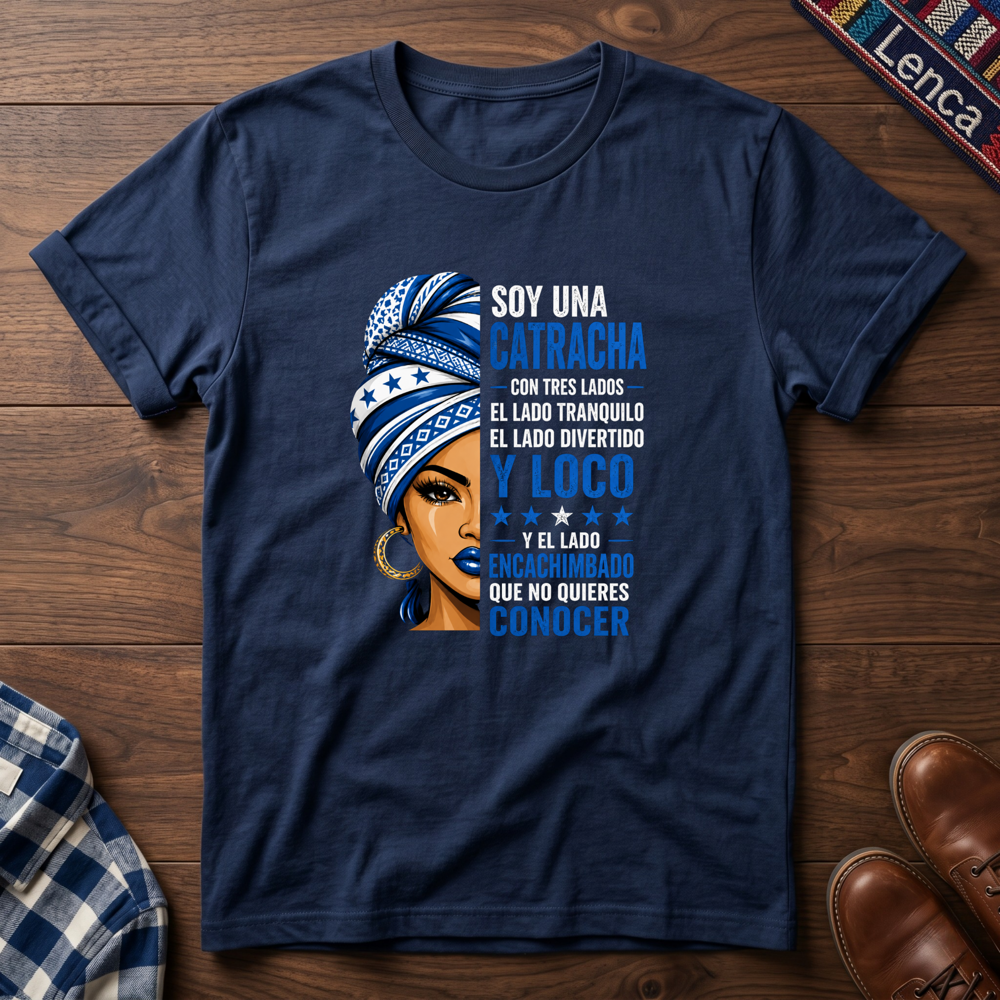 Navy blue t-shirt with a graphic of a woman with a headwrap and 'Soy Una Catracha' text on a wooden surface.
