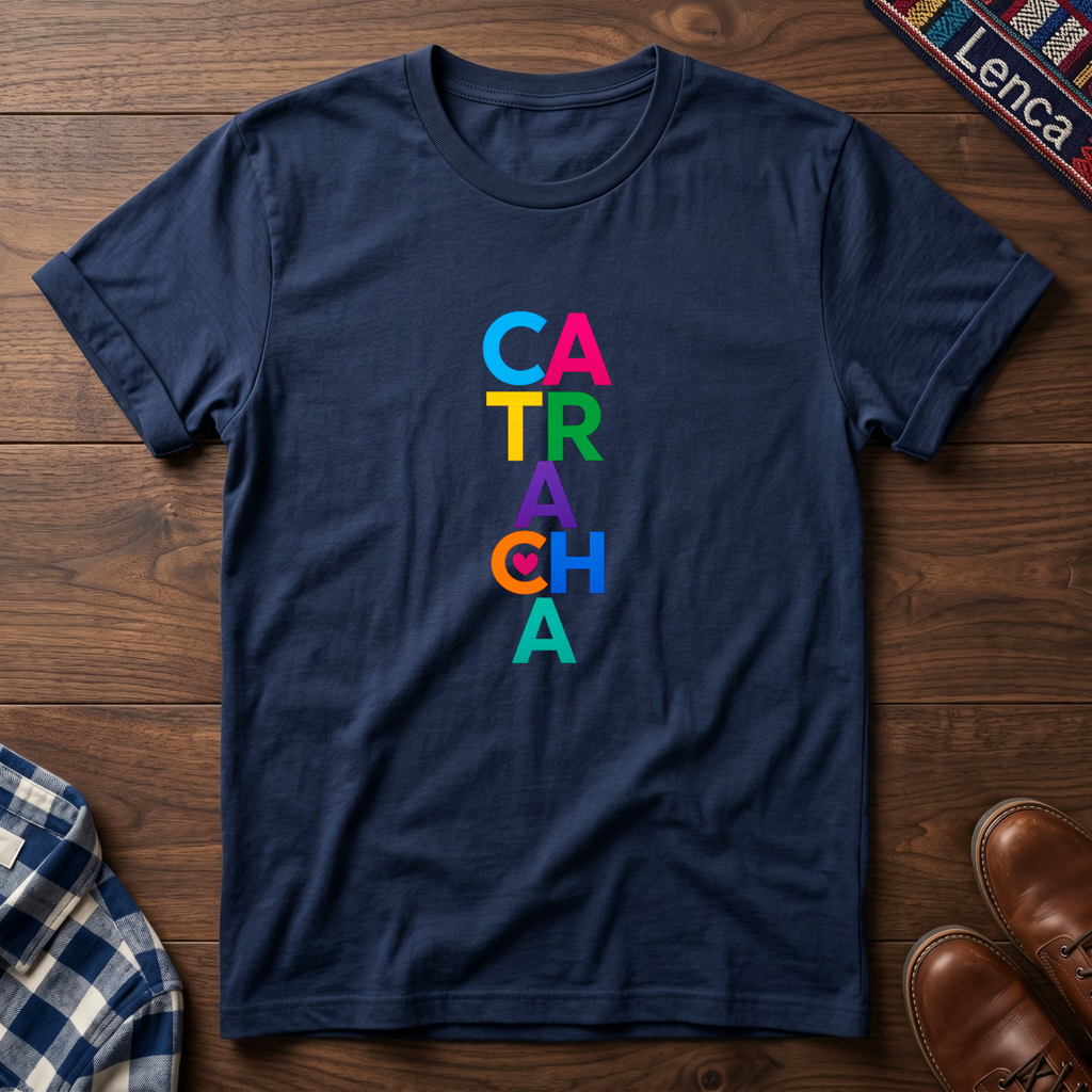 A navy blue short-sleeve t-shirt laid flat on a dark wood background, featuring the word 'CATRACHA' printed vertically in colorful letters (blue, pink, yellow, green, purple, orange, teal).