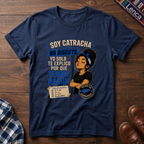 A navy graphic t-shirt laid flat on a dark wood background, featuring a printed design with the text 'SOY CATRACHA NO DISCUTO'.