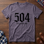 Paragon crewneck t-shirt with a black gothic-style graphic reading '504 CATRACHO' laid flat on a dark wood background.