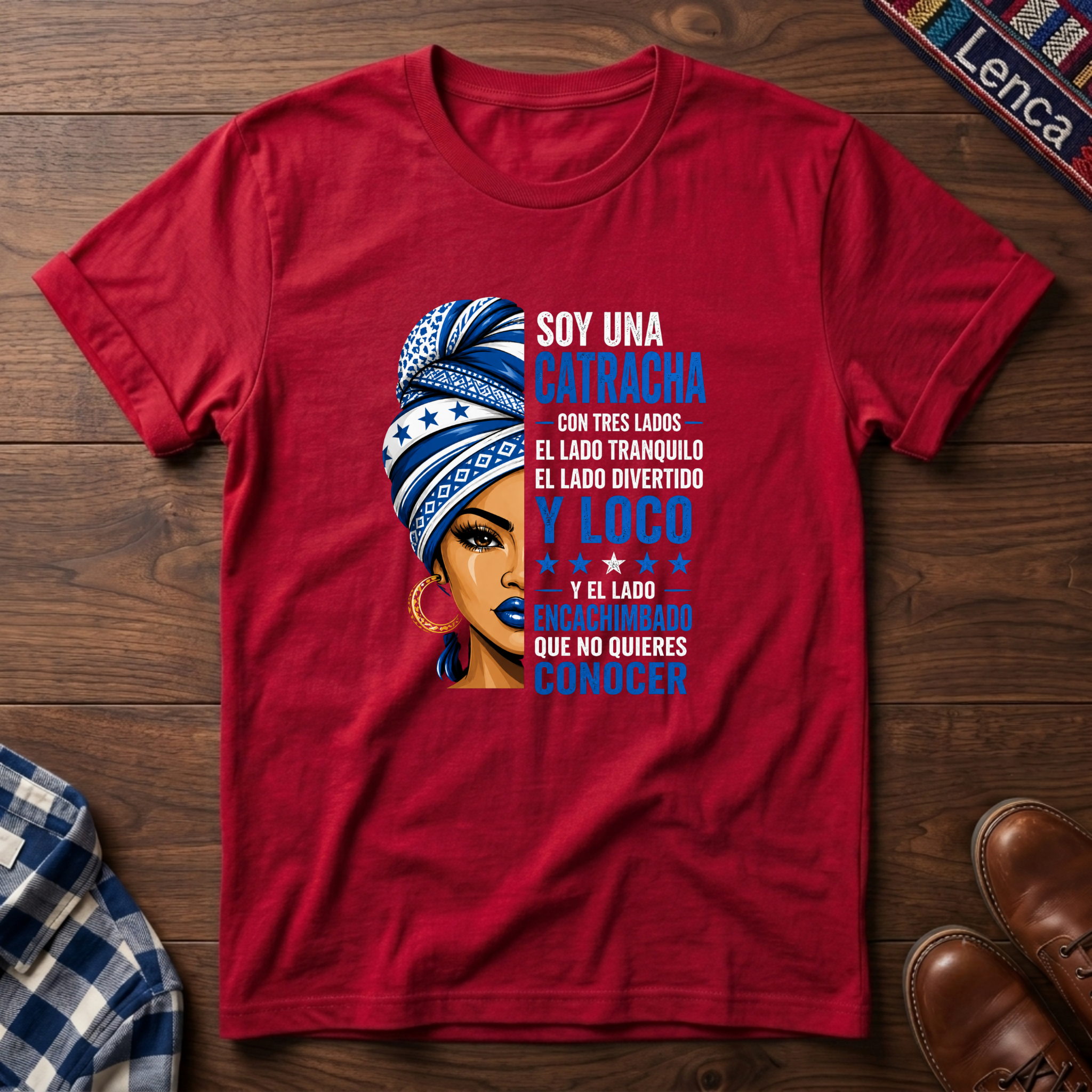Red t-shirt with a graphic of a woman with a headwrap and 'Soy Una Catracha' text on a wooden surface.