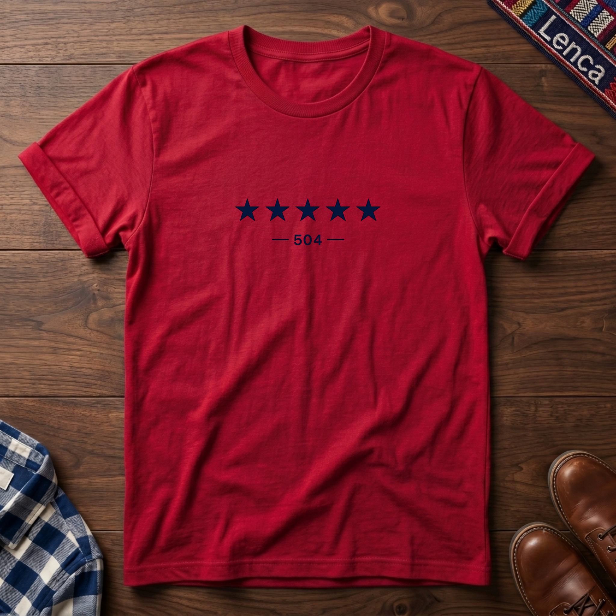 A red short-sleeve crewneck t-shirt with a graphic of five dark blue stars and the text '— 504 —' on the chest, laid flat on a wooden surface.