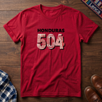 A red t-shirt laid flat on a wooden surface, featuring the text 'HONDURAS 504' printed on the chest. The numbers '504' are filled with a red, white, and blue pattern resembling the Honduran Lempira, while 'HONDURAS' is printed in black.