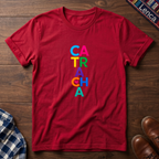 A red short-sleeve t-shirt laid flat on a dark wood background, featuring the word 'CATRACHA' printed vertically in colorful letters (blue, pink, yellow, green, purple, orange, teal).