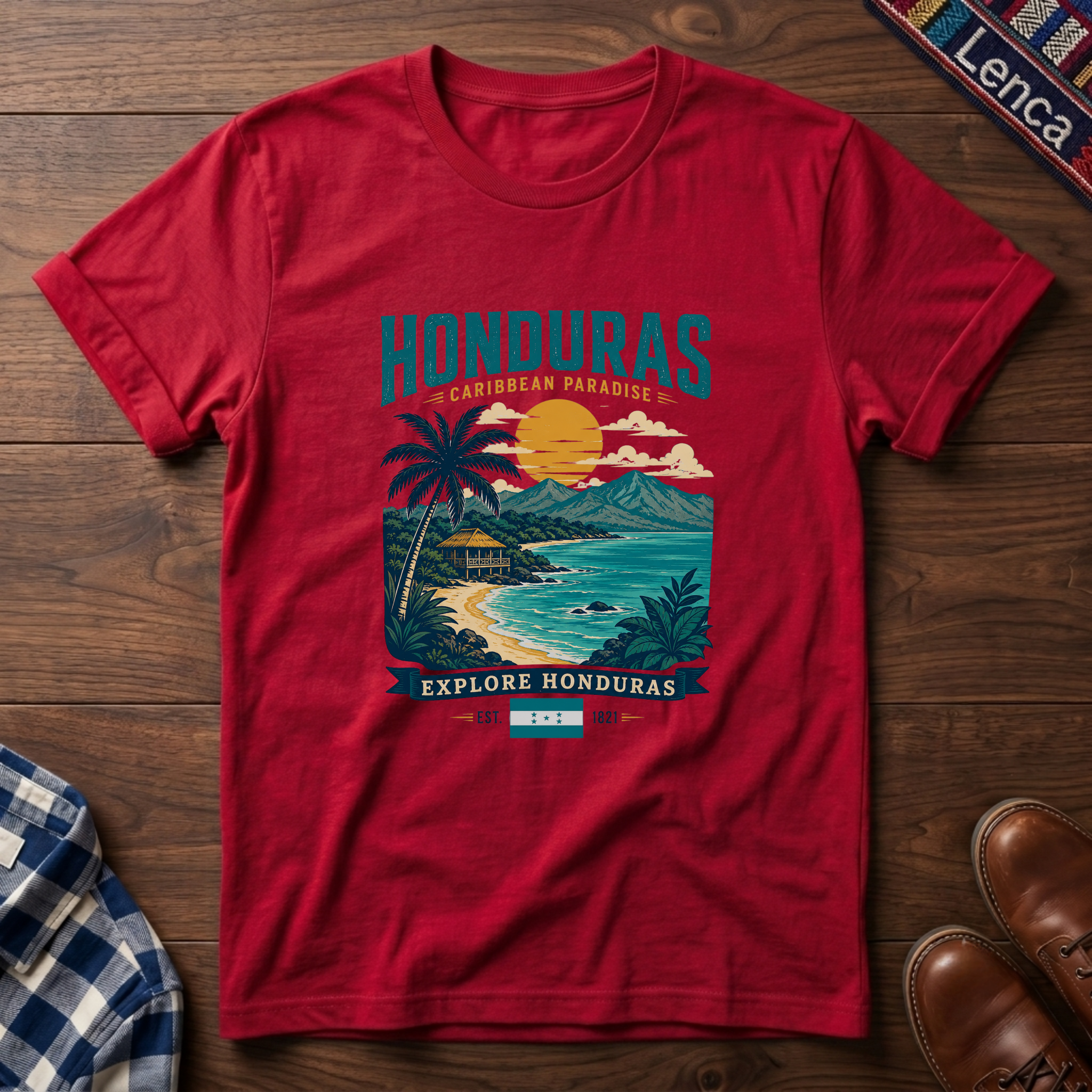 A red short-sleeve graphic t-shirt laid flat on a dark wood background, featuring a colorful tropical Honduras travel-style print with palm trees, a beach, ocean, and sunset. 