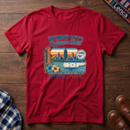 A red short-sleeve graphic t-shirt laid flat on a dark wood background, featuring a colorful vintage-style Chicago skyline and 'Windy City Catracho Heart' print.