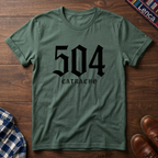 Military green t-shirt with '504 Catracho' text on a wooden surface.