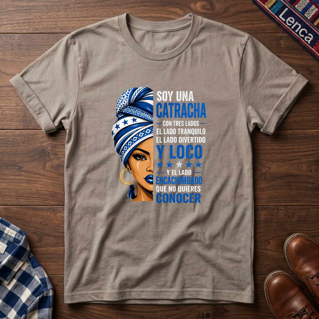 Sand t-shirt with a graphic of a woman with a headwrap and 'Soy Una Catracha' text on a wooden surface.