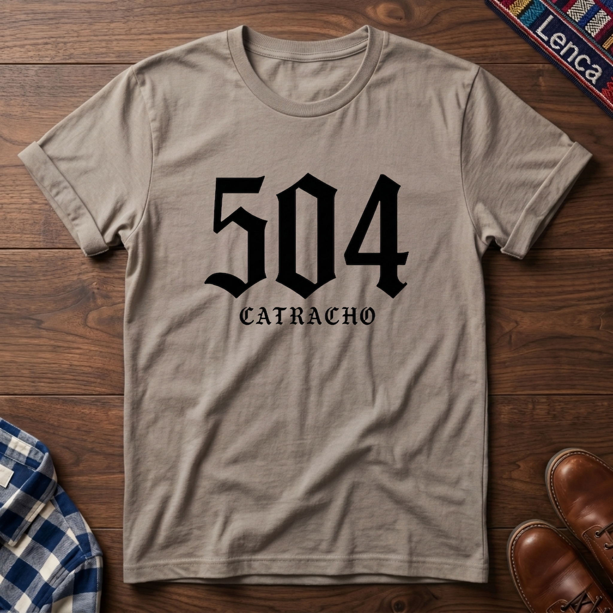Sand t-shirt with '504 Catracho' text on a wooden surface. 