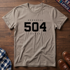 A sand crewneck t-shirt with a black graphic print reading 'HONDURAS 504' and five stars, laid flat on a dark wood background.