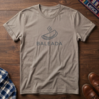 Sand t-shirt with 'Baleada' text and a baleada graphic design on a wooden surface.