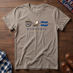 Sand t-shirt with 'Honduras' text and a Cafe Baleada Bandera graphic design on a wooden surface.