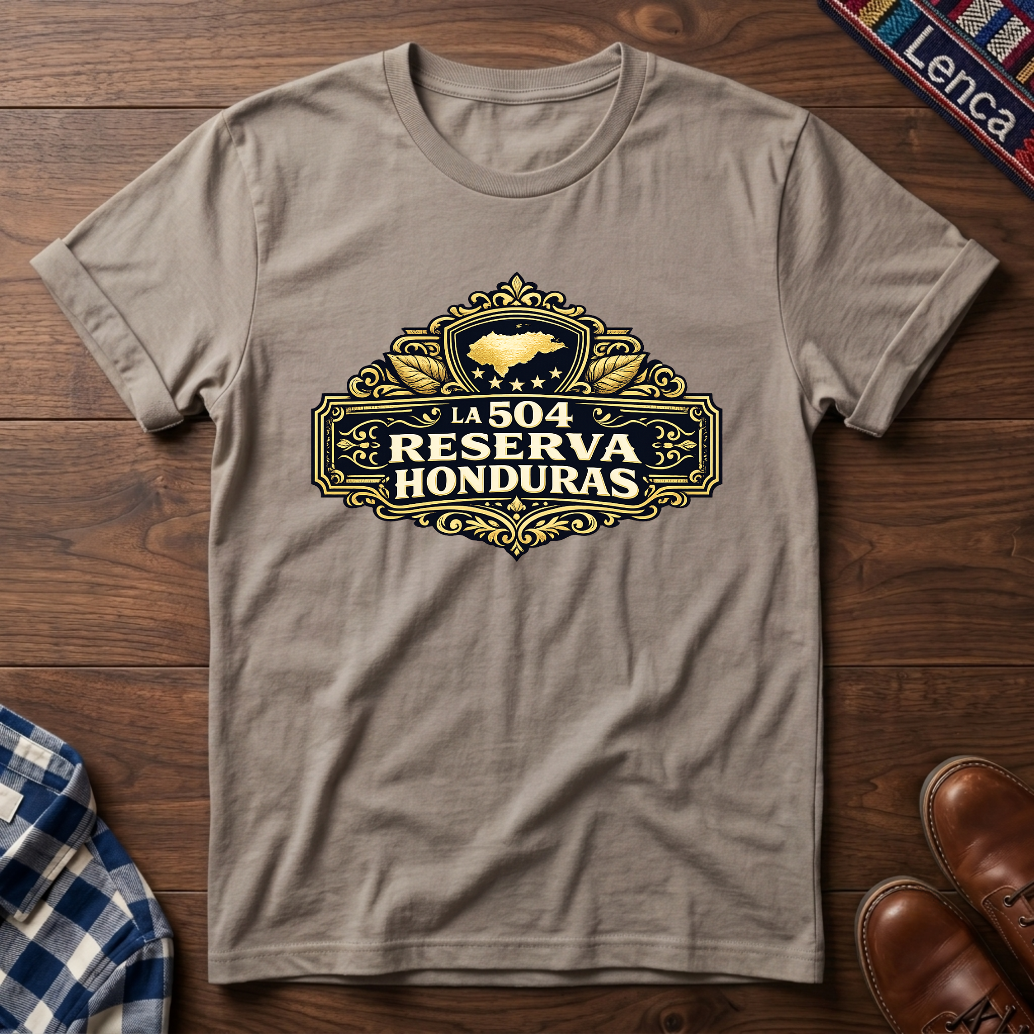 Sand t-shirt with 'La 504 Reserva Honduras' graphic design on a wooden surface.