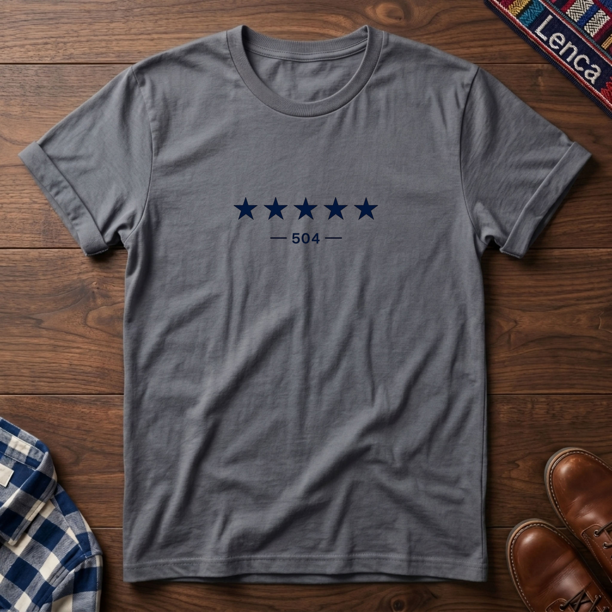 A sport gray short-sleeve crewneck t-shirt with a graphic of five dark blue stars and the text '— 504 —' on the chest, laid flat on a wooden surface.