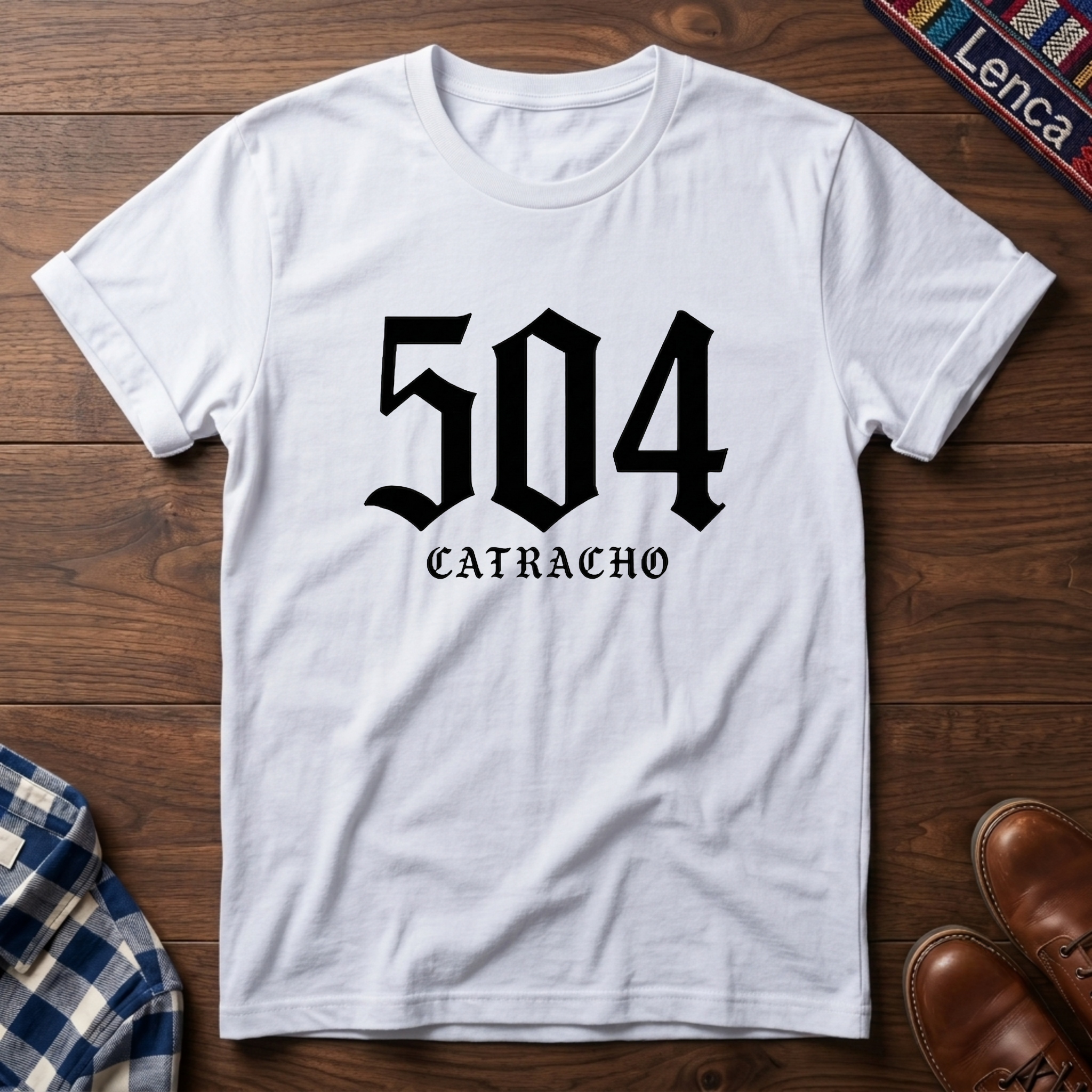 White t-shirt with '504 CATRACHO' printed on it, placed on a wooden surface.