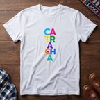 A white short-sleeve t-shirt laid flat on a dark wood background, featuring the word 'CATRACHA' printed vertically in colorful letters (blue, pink, yellow, green, purple, orange, teal).